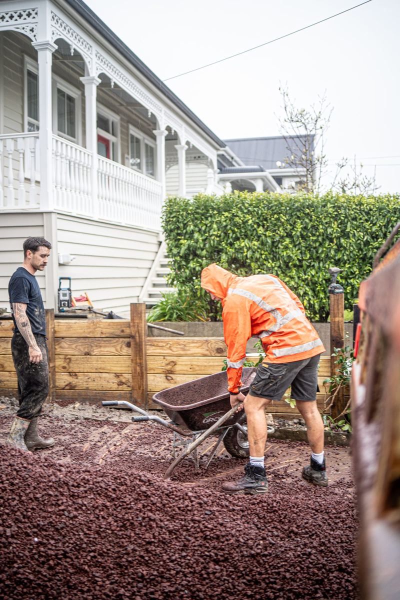 Crew backfilling a new timber retaining wall with scoria in the rain